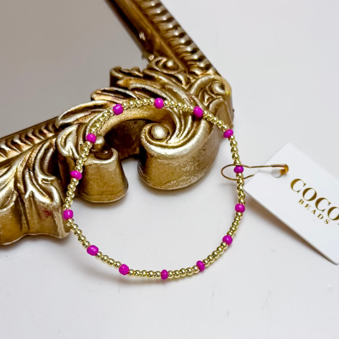 Gold bracelet with pink beads on a decorative gold frame, featuring a &