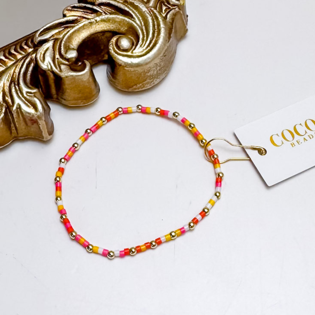 Beaded necklace with pink, yellow, and gold beads on a white surface with a decorative gold object.
