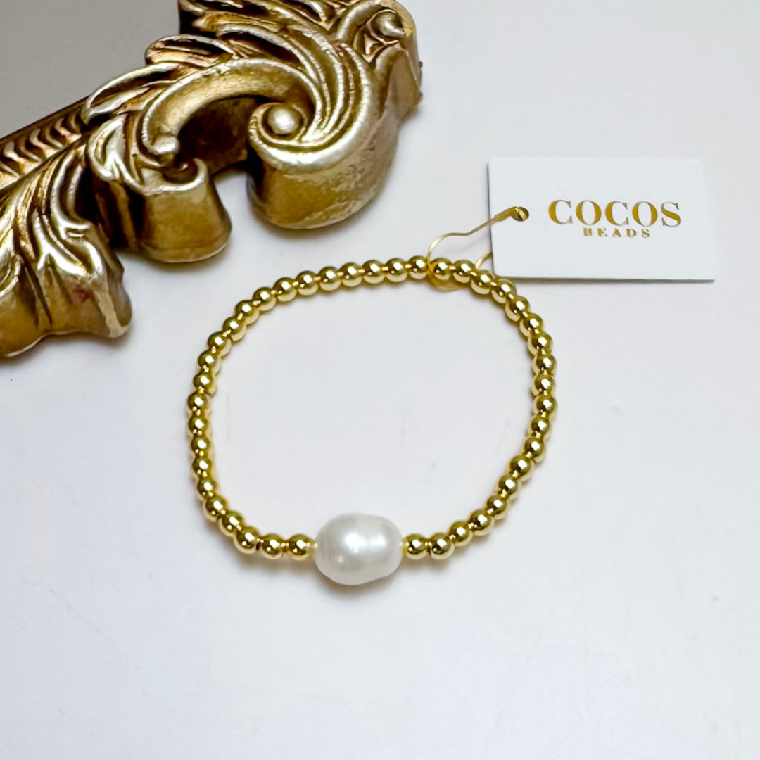 Gold bracelet with a pearl on a white surface, branded &
