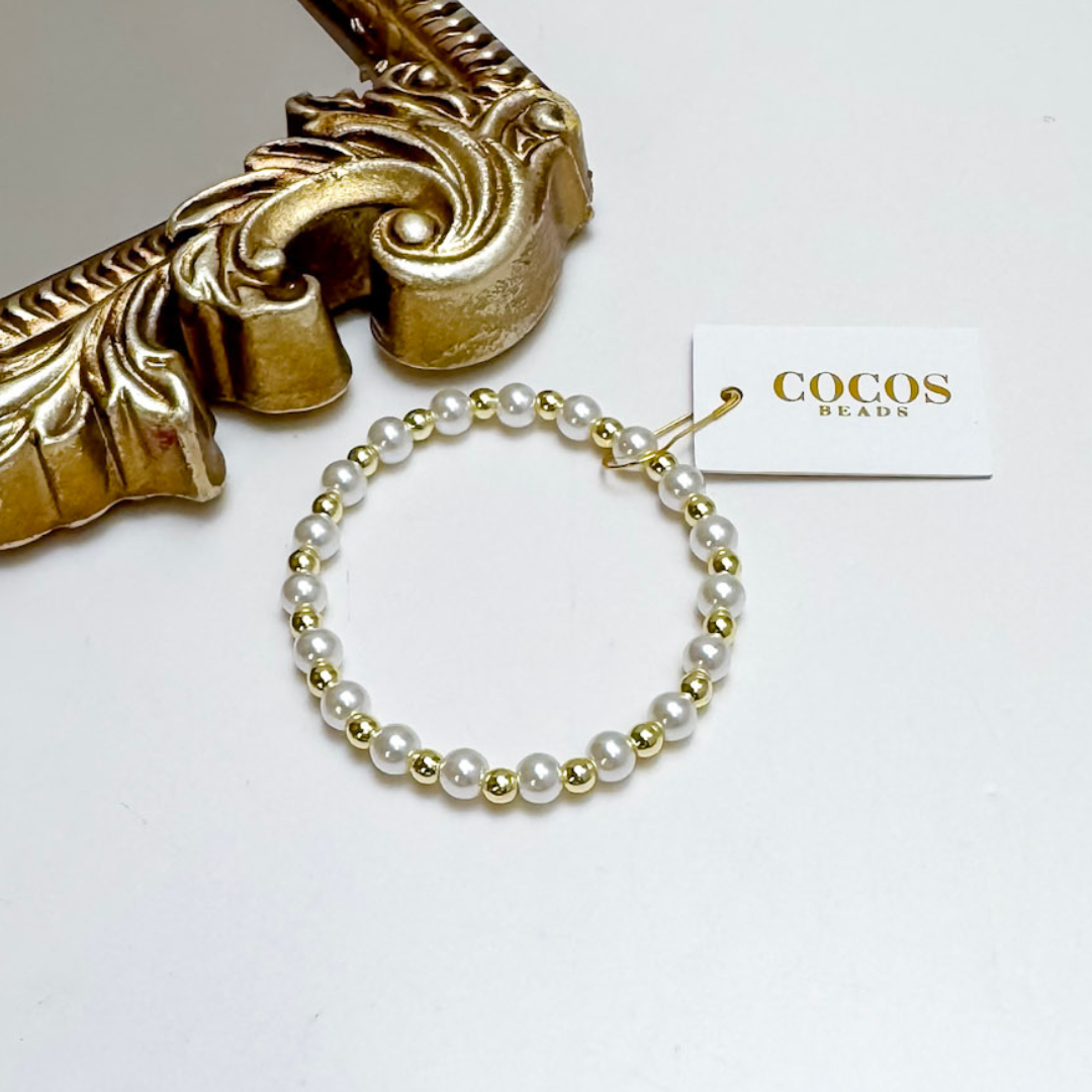 Pearl bracelet with gold accents on a white surface next to a decorative gold object, with &