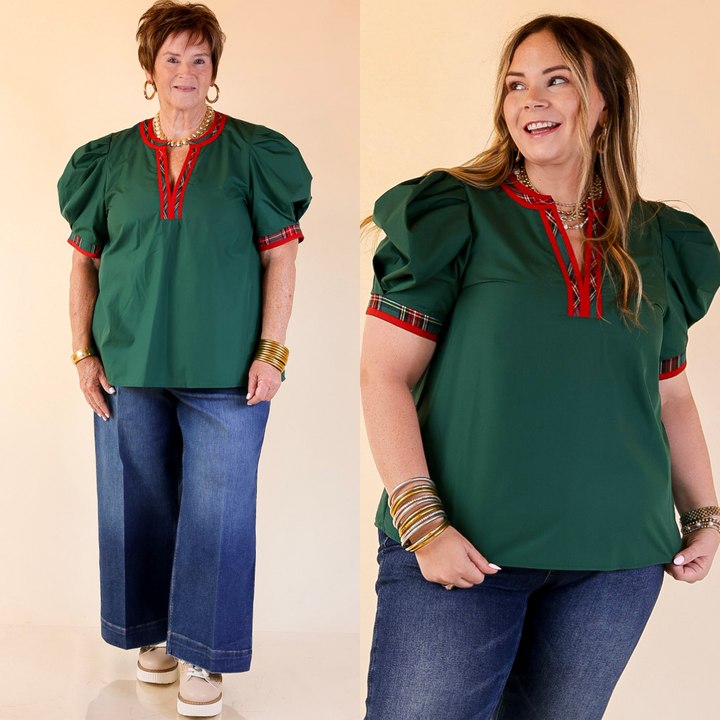 Two women wearing green tops with red accents and blue jeans on a beige background