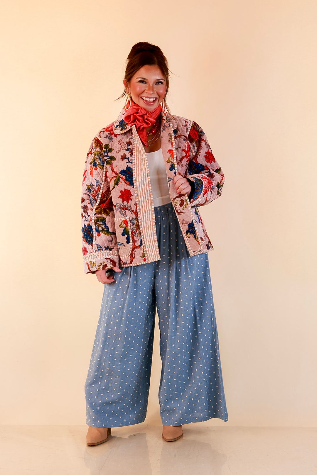 Model wearing light blue polka dot wide-leg pants with a blush pink quilted floral jacket, white top and tan booties.