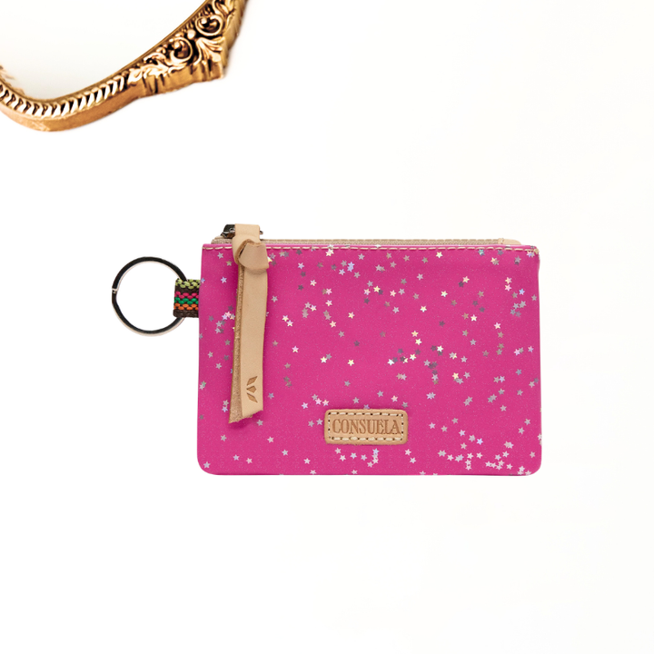 A pink zippered pouch with silver glitter stars, featuring a tan leather tab and a key ring, on a white background with a gold ornate frame partially visible in the top left corner.