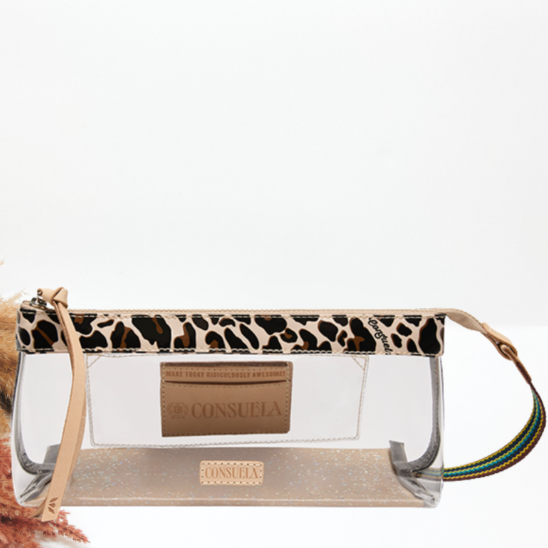 A Consuela clear plastic pouch bag with a leopard print faux-leather trim, a tan leather brand patch, and a multicolor braided strap, shown on a white background.