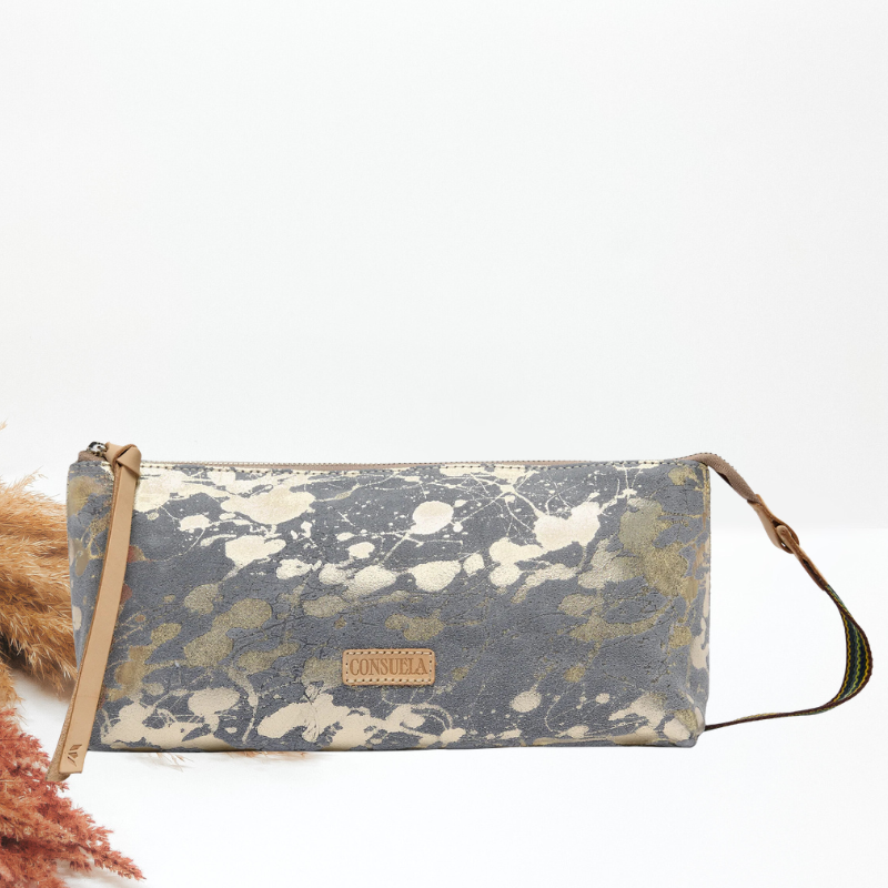 A rectangular Consuela zip pouch with a gray and beige splatter pattern, a tan leather wristlet strap, and a woven crossbody strap.
