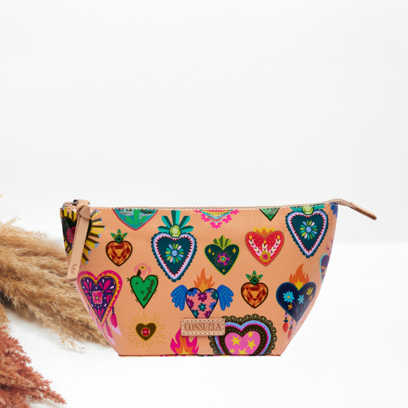 A peach cosmetic bag with a colorful folk-art heart print, a tan leather zipper pull and wrist strap, and a Consuela leather brand plate.