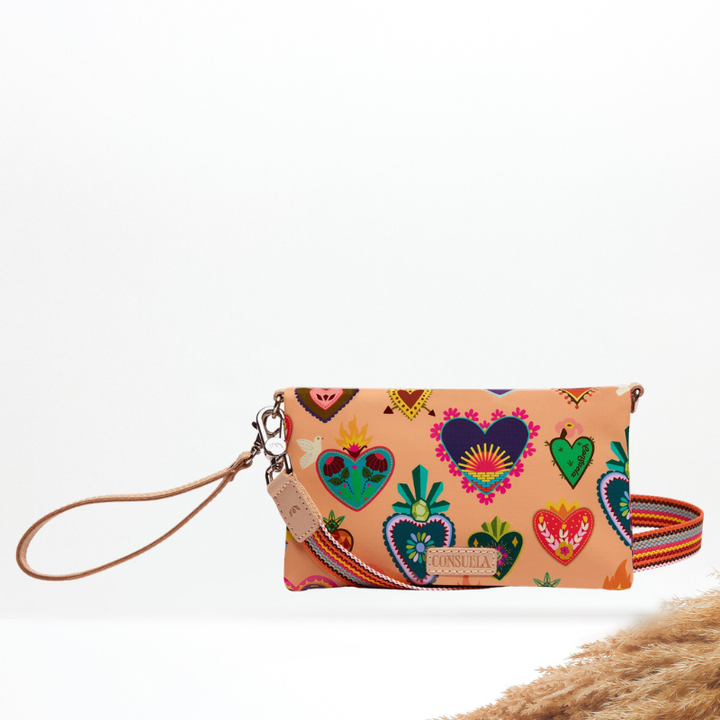 A small peach wristlet pouch with colorful embroidered heart motifs, a tan wrist strap, a matching patterned crossbody strap, and a Consuela leather brand patch on the front.