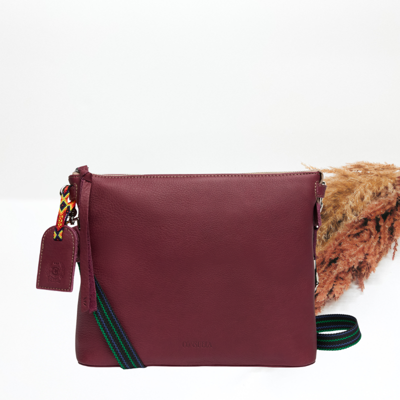 Maroon leather handbag with colorful strap on a white background