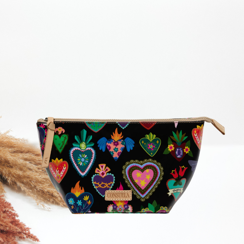 A black cosmetic bag with a colorful folk-art heart print, a tan leather zipper pull, and a Consuela leather brand plate.