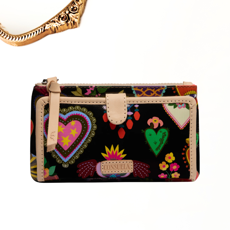 A rectangular black zip-around wallet with a colorful Mexican folk art print featuring hearts, flowers, and birds, finished with beige leather trim and a matching zipper pull.