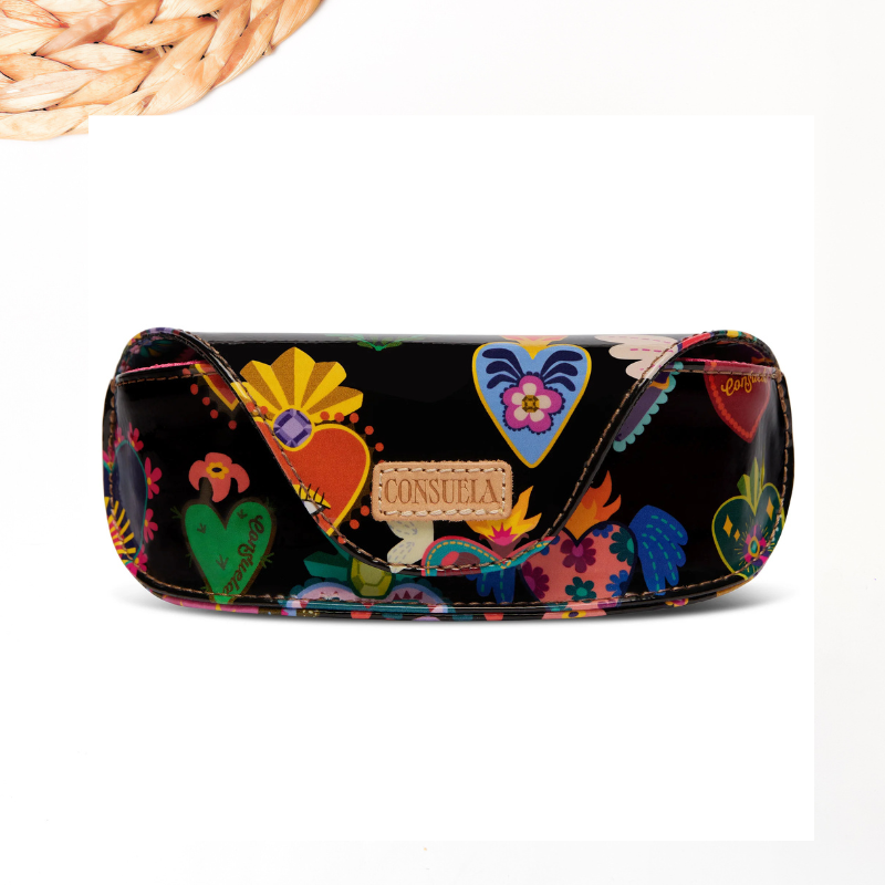 A black leather glasses case decorated with colorful Mexican folk art motifs, including hearts, flowers, and a central tan leather patch with the brand name 'CONSUELA' in script. The case is displayed on a clean white background with a decorative woven straw element in the top-left corner.