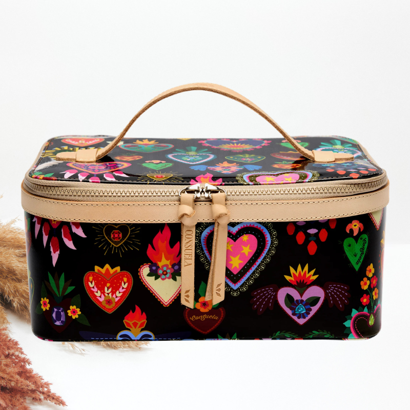 A rectangular black Consuela train case with a colorful heart and floral folk-art pattern, featuring a tan leather handle and zipper pull tabs.