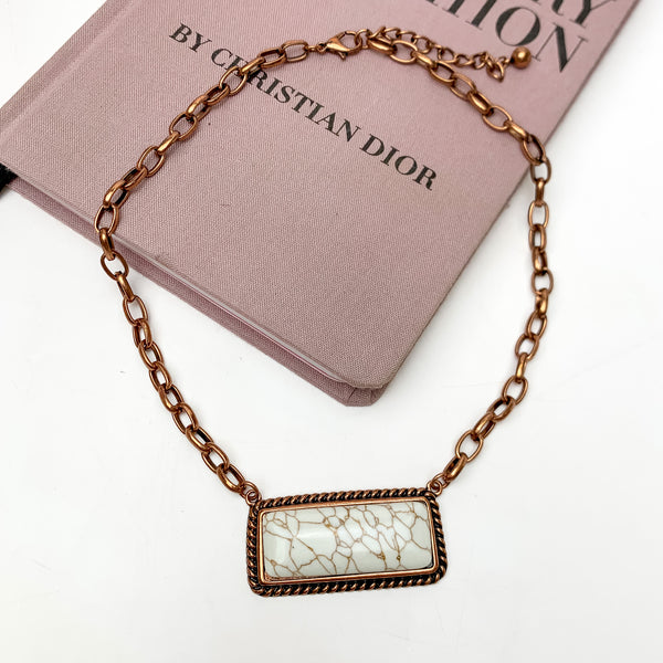 Copper Tone Necklace With Marbled Rectangle Pendant. This necklace is pictured on a white background with part of it on a pink book.