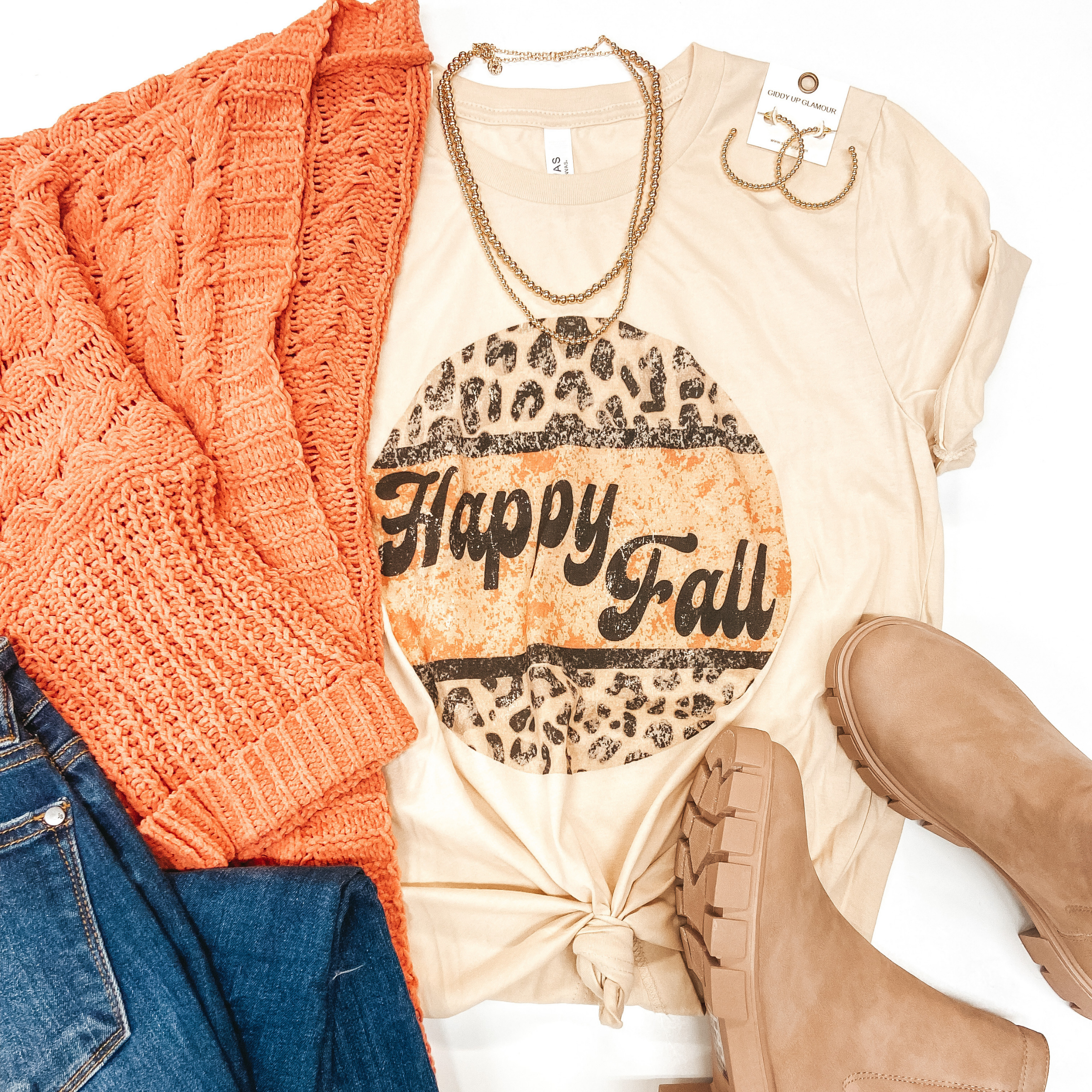 Beige crew neck tee shirt with leopard and orange circle that says "Happy Fall" inside. Pictured with orange cardigan, jeans, booties, and gold jewelry. 