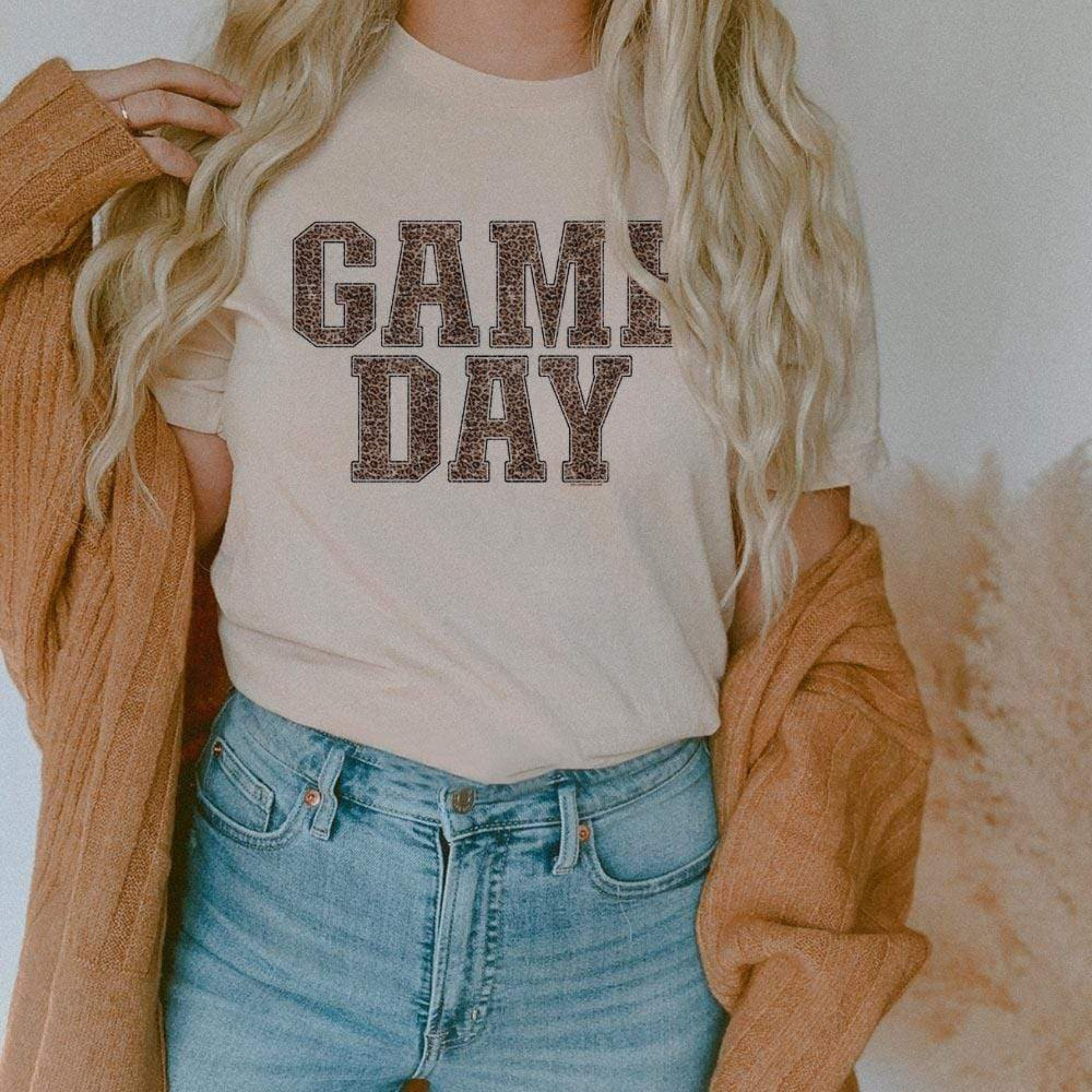 Model is wearing a cream colored short sleeve crewneck tee featuring a leopard print graphic that says "Game day"
