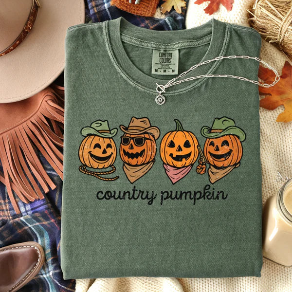 Folded green t-shirt with 'country pumpkin' design and pumpkins wearing hats on a rustic background.