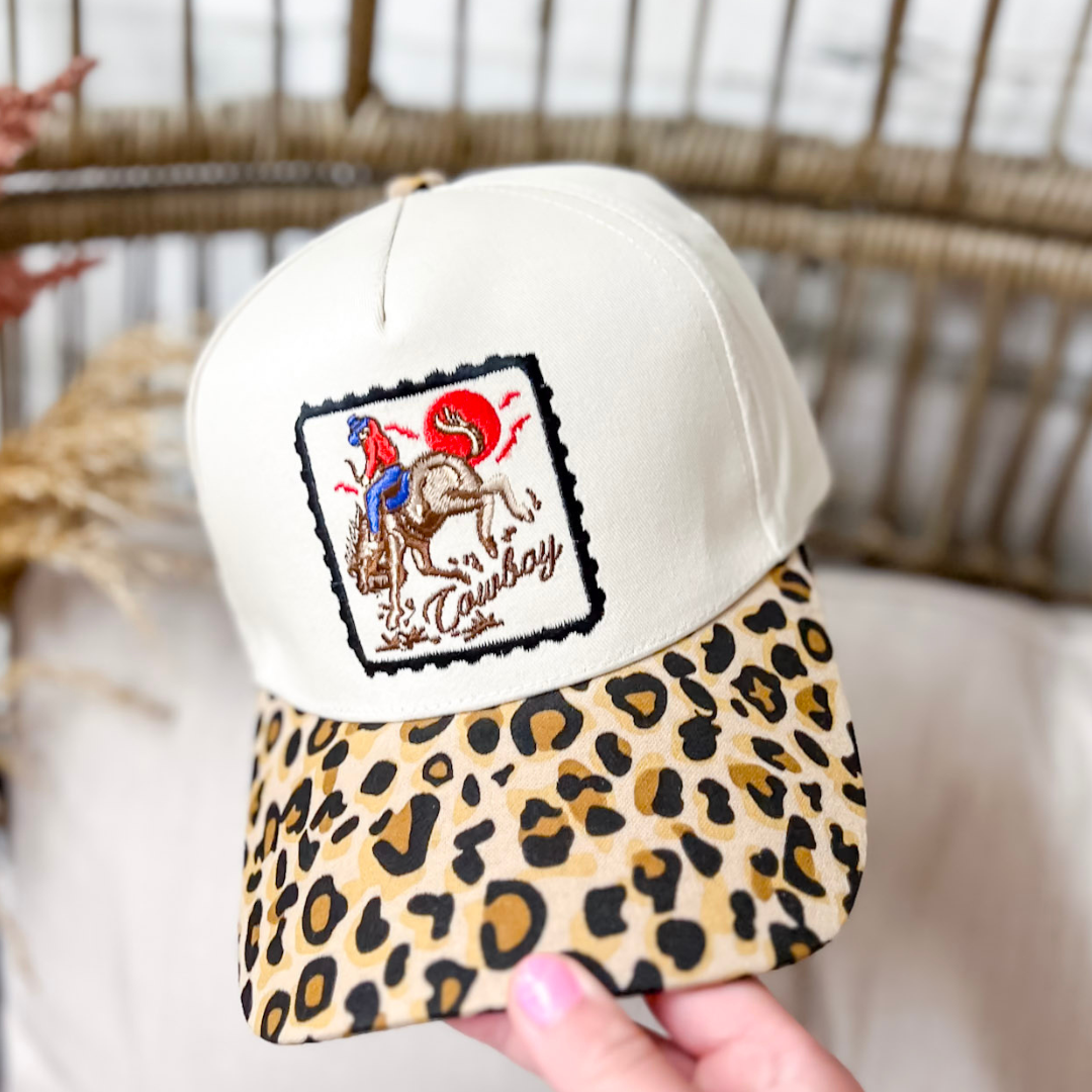 Cowboy Horse Two-Tone Canvas Trucker Cap in Leopard featuring a cream canvas crown, vintage embroidered cowboy riding a bucking horse patch, leopard-print brim, and adjustable snapback closure.