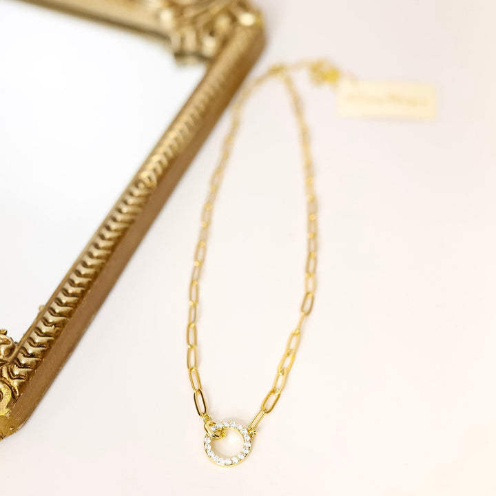 Gold necklace on a white surface with a gold frame in the background