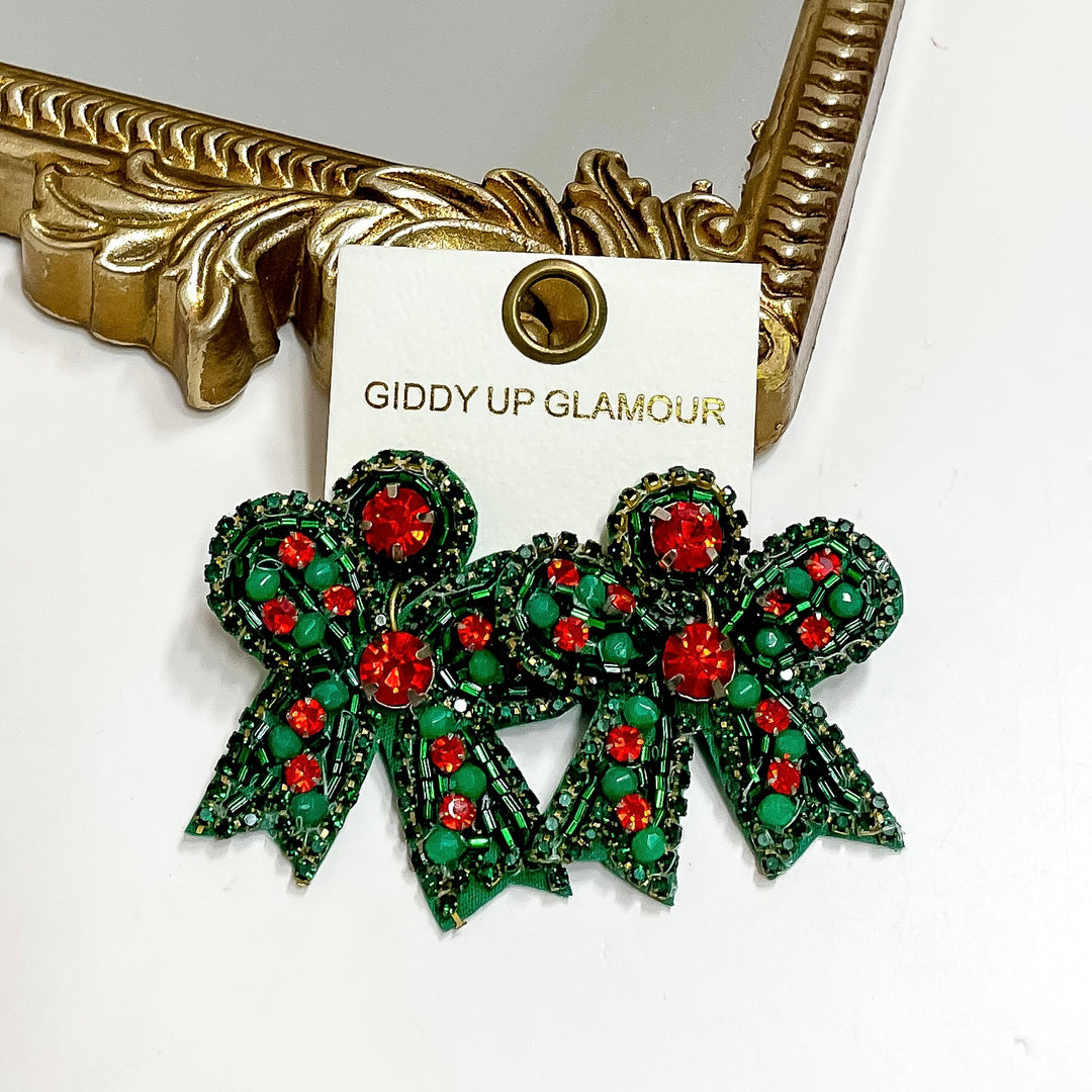Green and red bow-shaped earrings on a 'Giddy Up Glamour' card with a gold frame in the background.