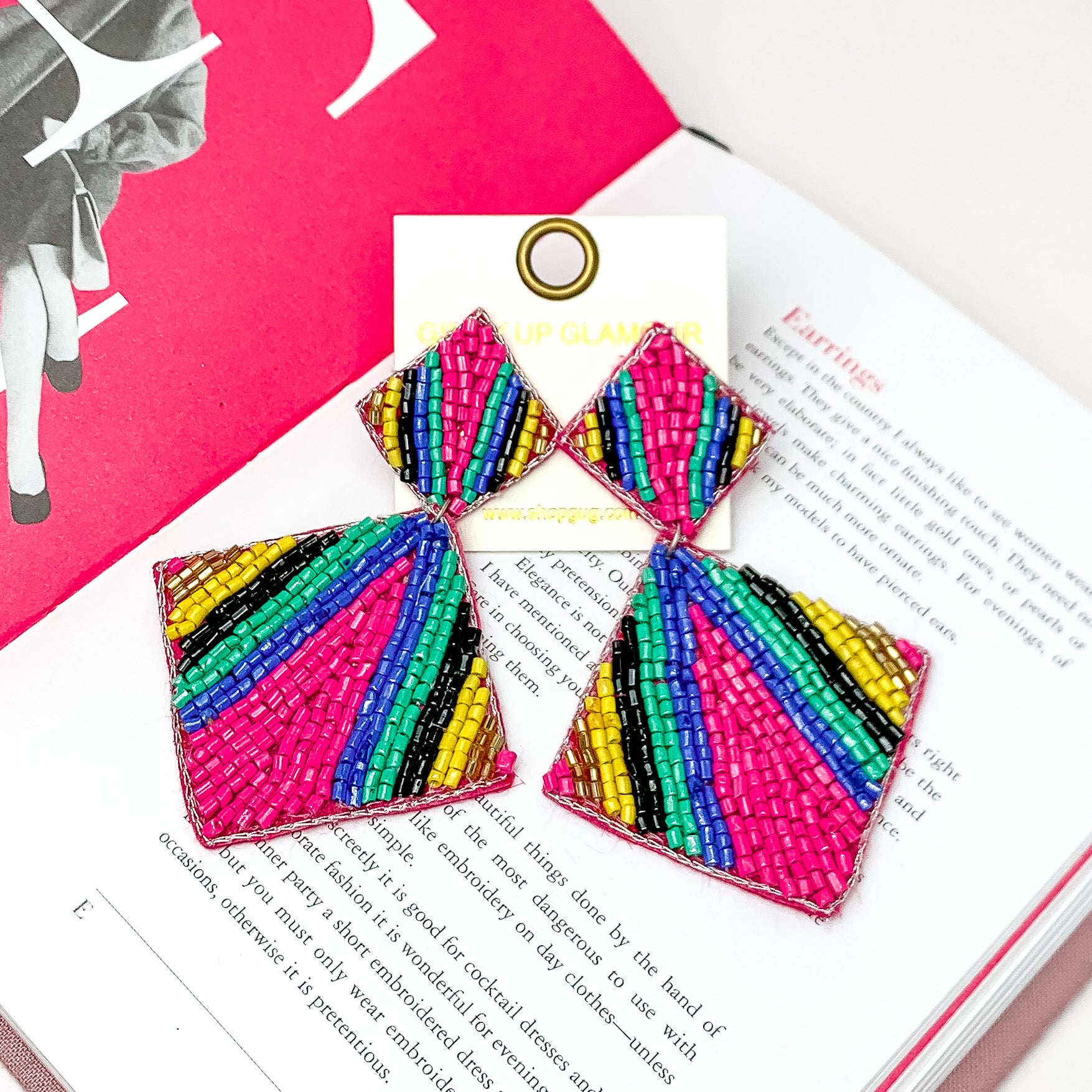 Beaded Double Diamond Striped Earrings in Multicolor. Pictured on a white background with an open book behind the earrings. 