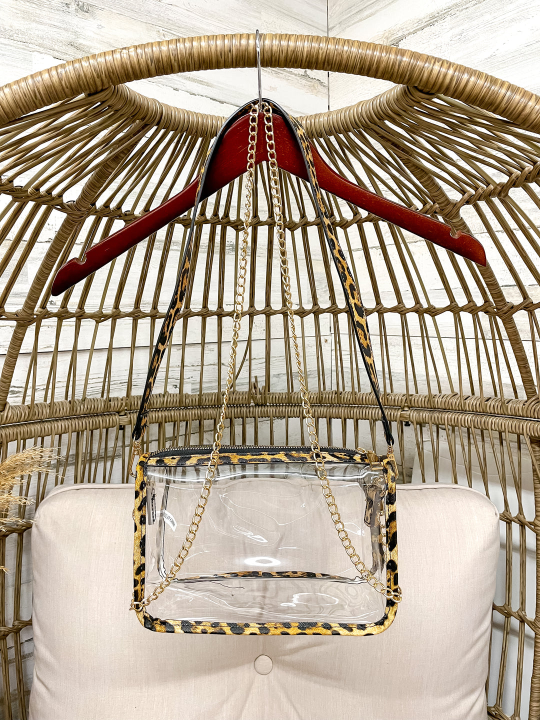 Clear handbag with leopard print trim on a red hanger against a wicker chair background