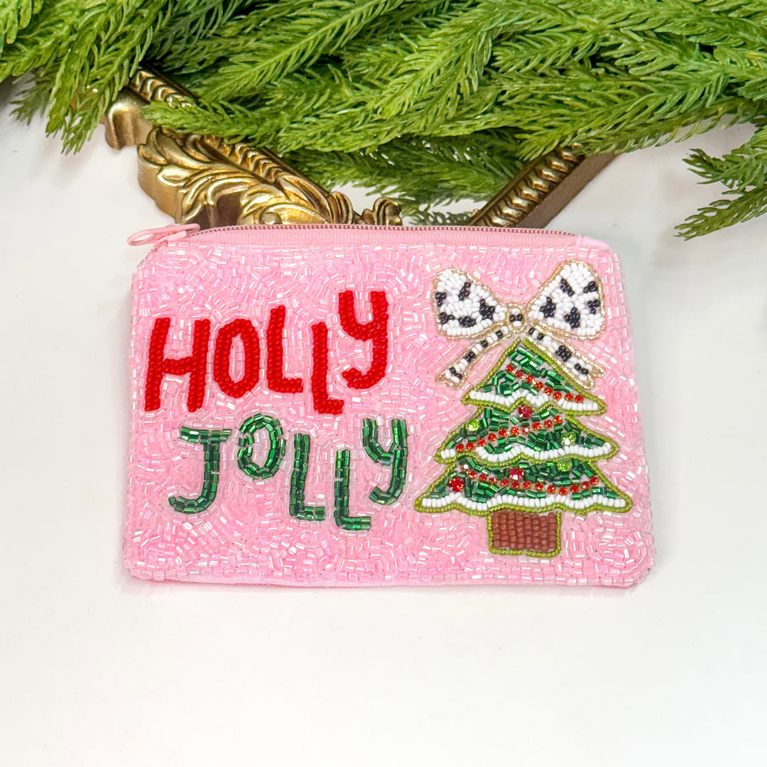 Pink beaded pouch with 'Holly Jolly' text and Christmas tree design, placed under a tree.