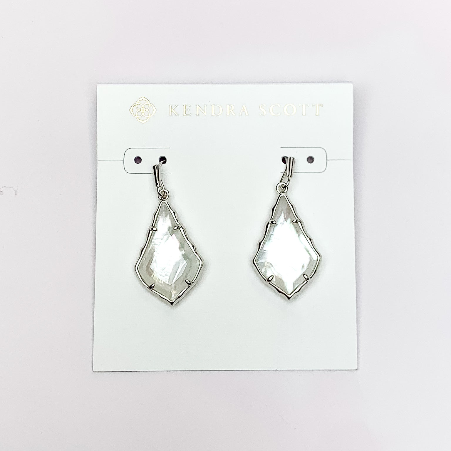 Silver outline drop earrings with an ivory mother of pearl stone. These earrings are pictured on a white earrings holder on a white background. 