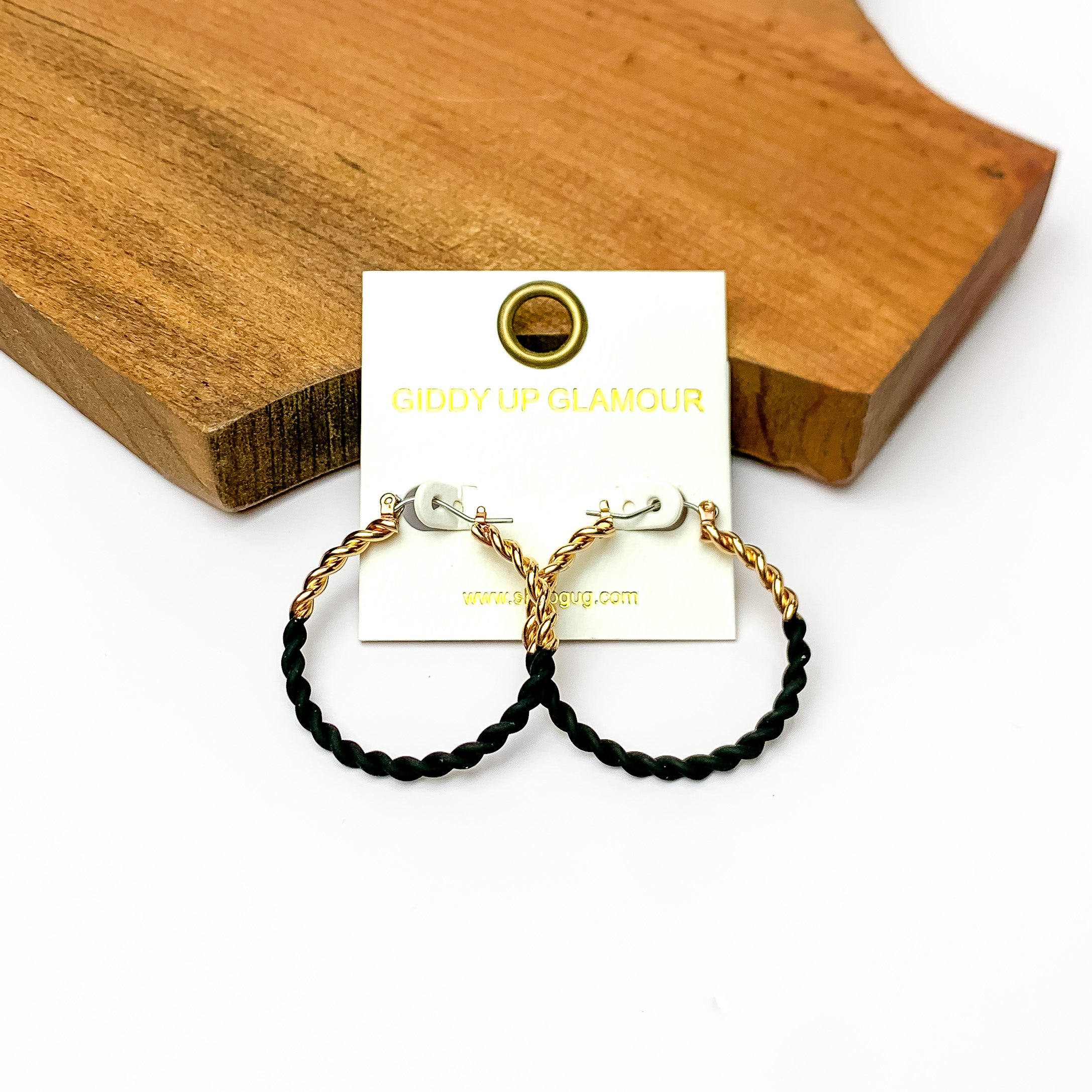 Twisted Gold Tone Hoop Earrings in Black. Pictured on a white background with a wood piece behind it.
