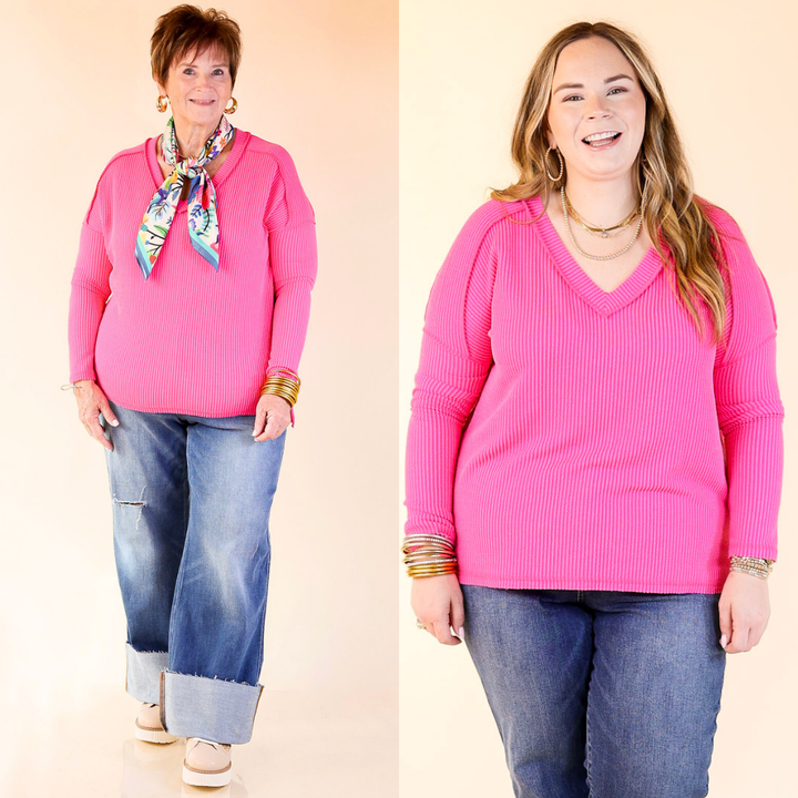 Two women wearing pink sweaters and blue jeans against a plain background