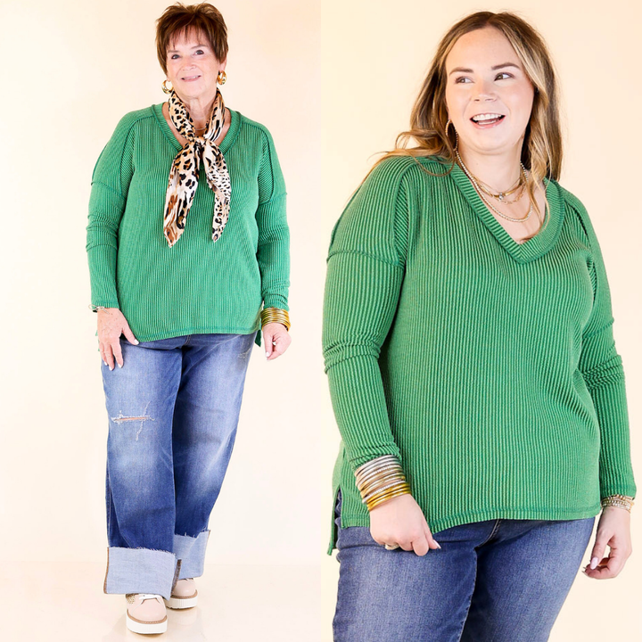 Two women wearing green sweaters and blue jeans against a plain background