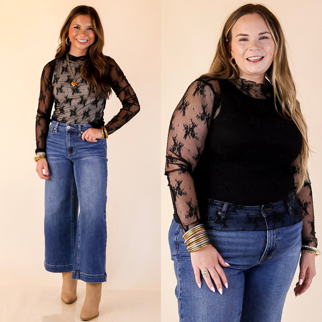 Two women wearing black lace tops and blue jeans on a beige background
