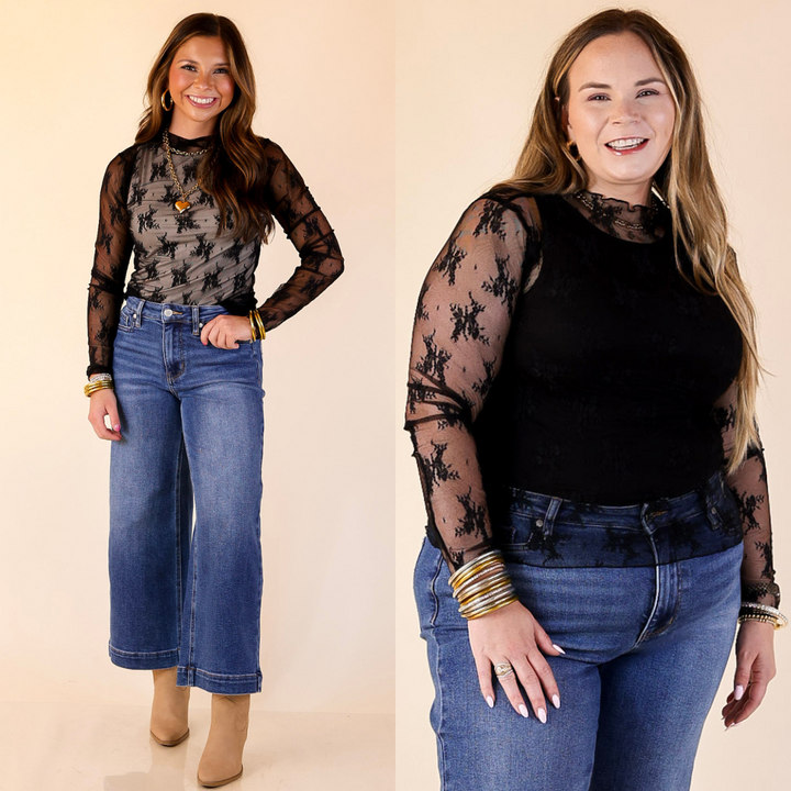 Two women wearing black lace tops and blue jeans on a beige background