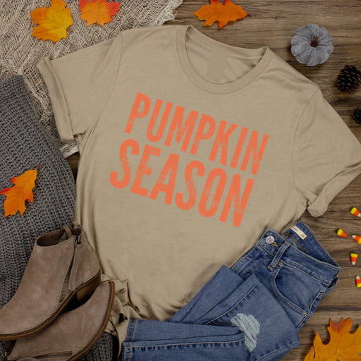Beige t-shirt with 'Pumpkin Season' text, paired with jeans, boots, and a sweater on a wooden surface with fall decorations.