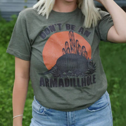 Woman wearing a t-shirt with a graphic armadillo design and text outdoors.