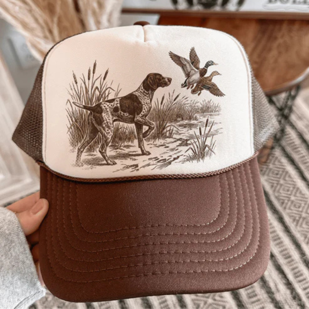 Brown and tan trucker hat featuring a vintage hunting dog and duck graphic with an adjustable mesh back.