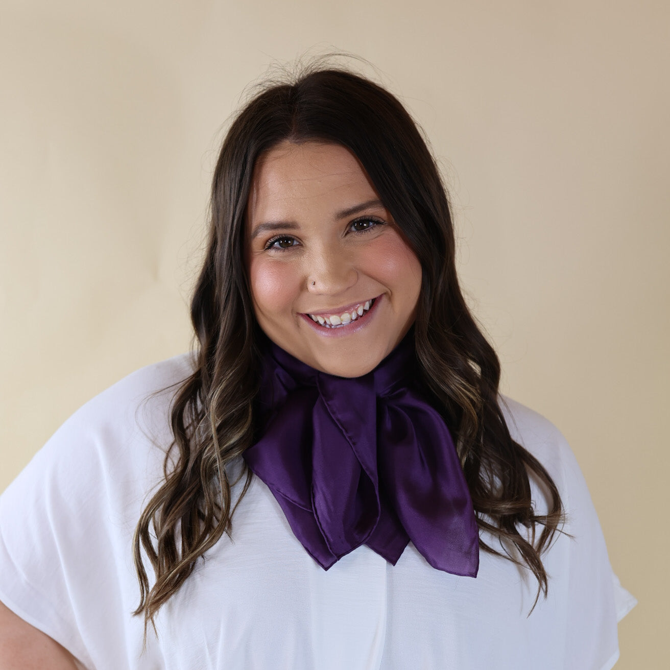 Brunette model is pictured wearing a White, Drop shoulder top with a Solid Purple scarf tied around her neck. Model is pictured in front of a beige background. 