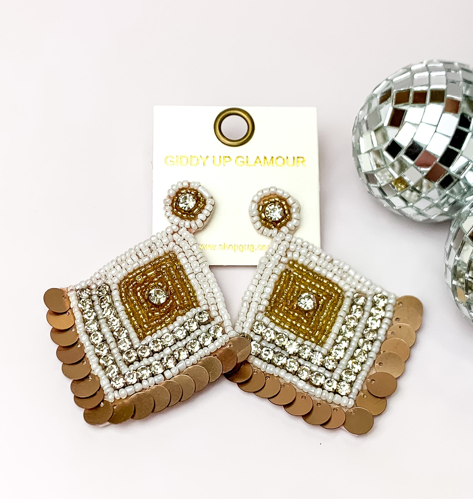 Fashionista Diamond Shaped Beaded Earrings in White, and Gold. Pictured on a white background with disco balls to the right.