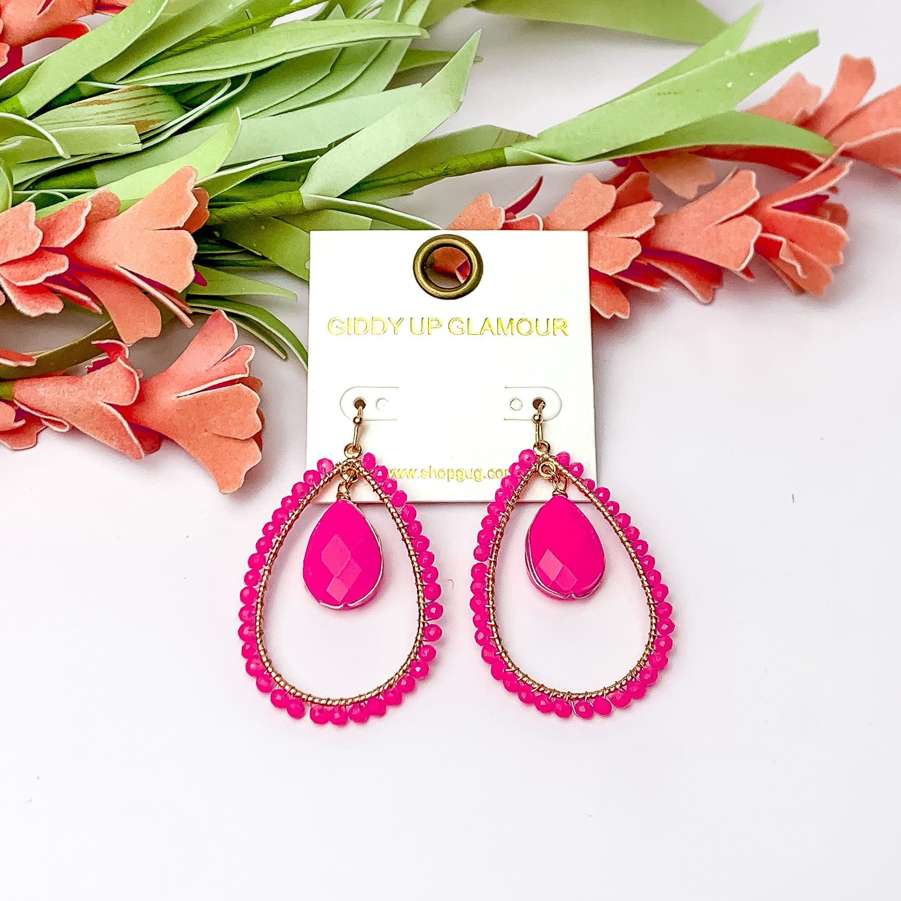 Pink Stone Inside Open Beaded Teardrop Earrings with Gold Tone Outline. Pictured on a white background with flowers at the top.