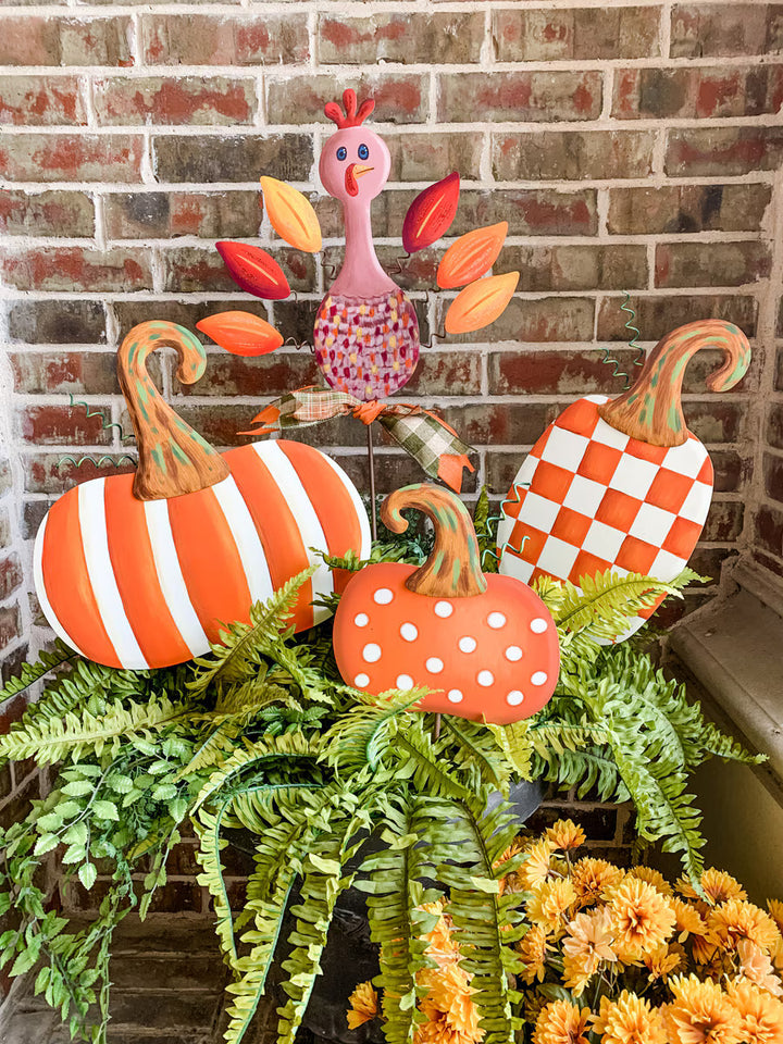 Round Top Collection orange patterned pumpkin decorations featuring striped, checkerboard and polka dot pumpkins styled in a fern-filled fall porch planter.