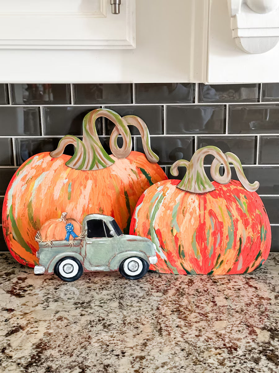 Large and small Orange Artful Pumpkins by The Round Top Collection displayed on a kitchen counter with colorful painted brushstrokes and curly stems.
