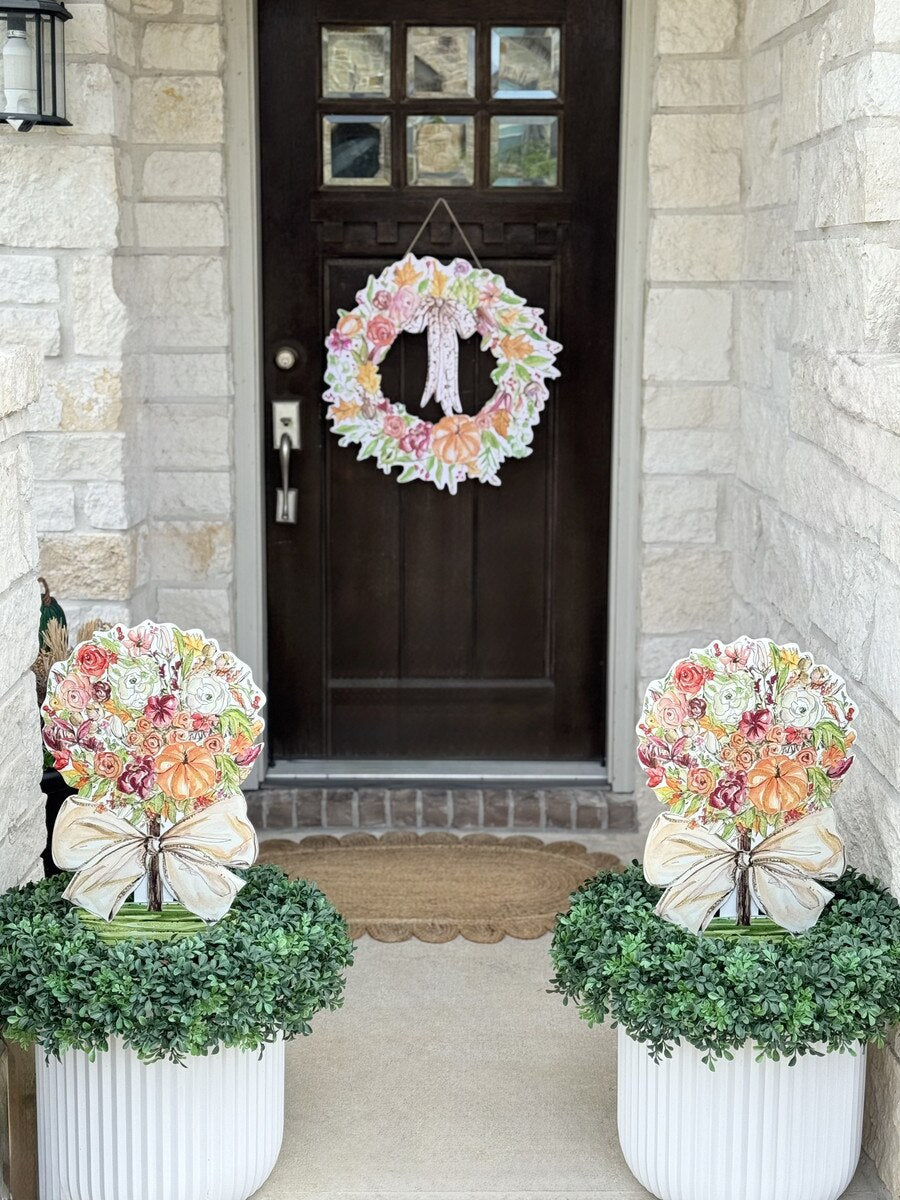 Two Rosanne Beck Rose and Pumpkin Topiary decorations displayed in green porch planters with coordinating colorful fall wreath on front door.