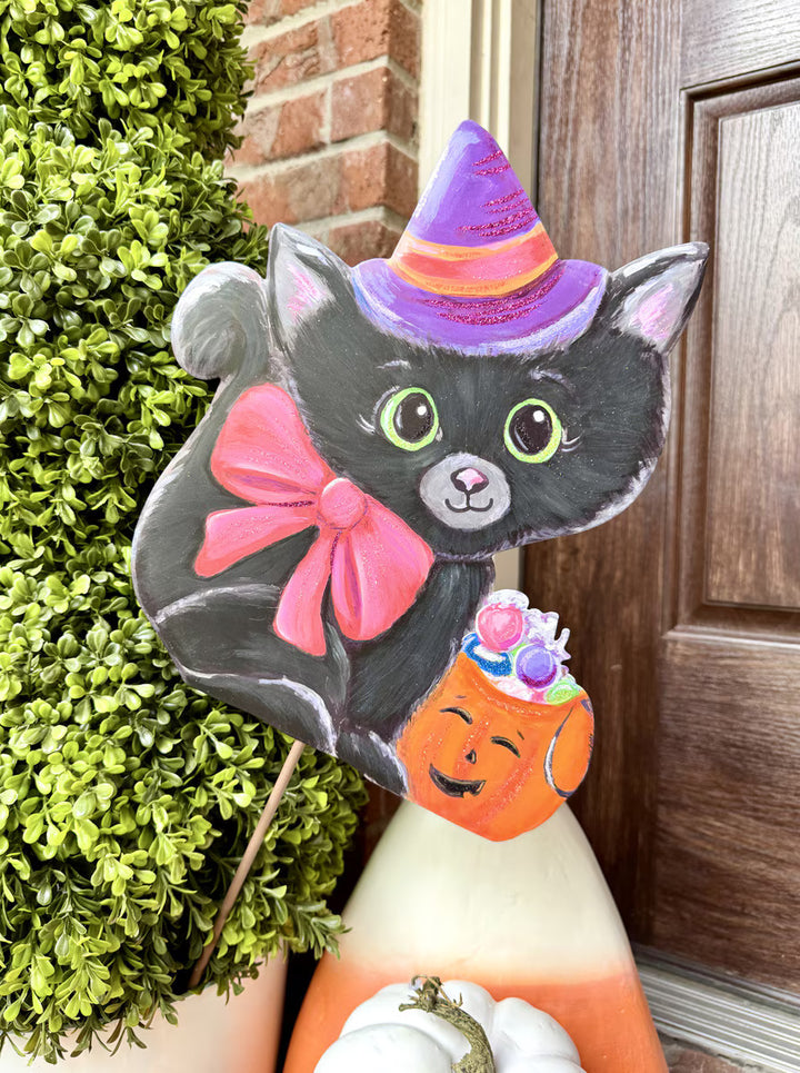 Sweet Kitty Witch metal Halloween garden stake featuring a black cat in a purple witch hat with a pink bow and orange candy bucket displayed in a porch planter.