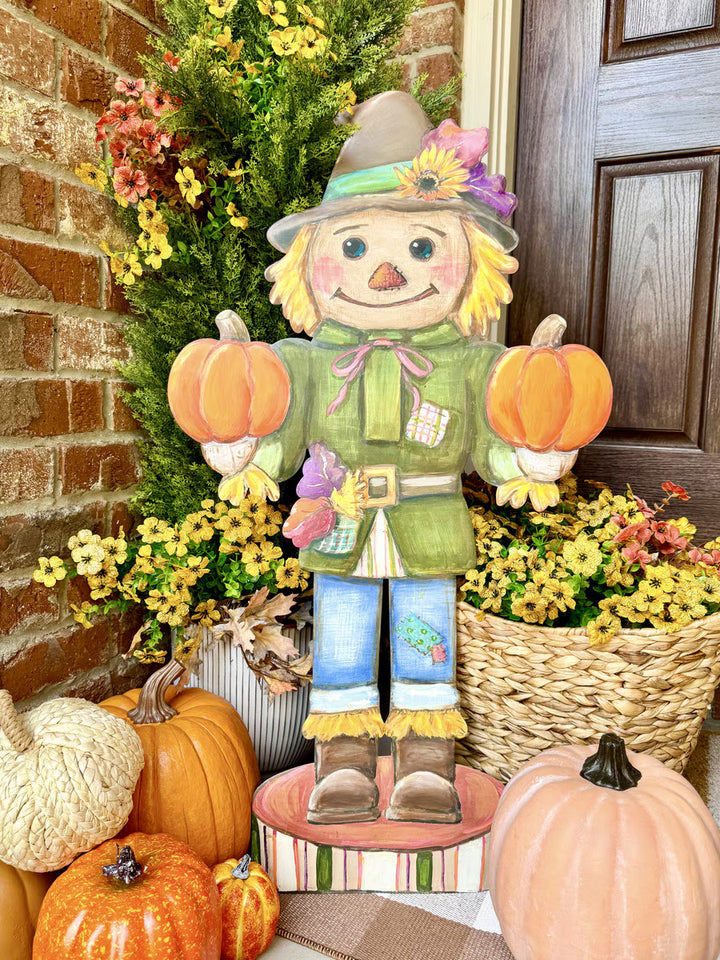 35.5-inch Scarecrow Nutcracker by Round Top Collection displayed with pumpkins, yellow fall flowers and greenery beside a front door.