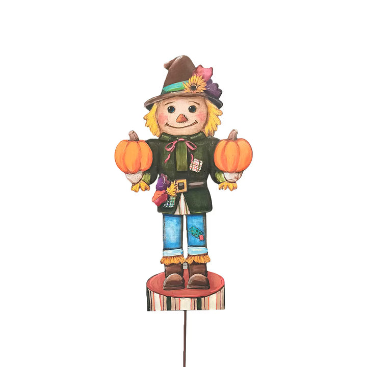 Small Scarecrow Nutcracker by Round Top Collection holding two orange pumpkins with green jacket, blue pants and colorful fall hat.