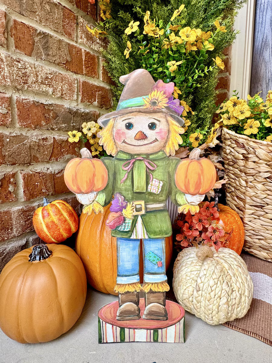 Small Round Top Collection Scarecrow Nutcracker styled on a fall porch with orange pumpkins, woven pumpkin and autumn flowers.
