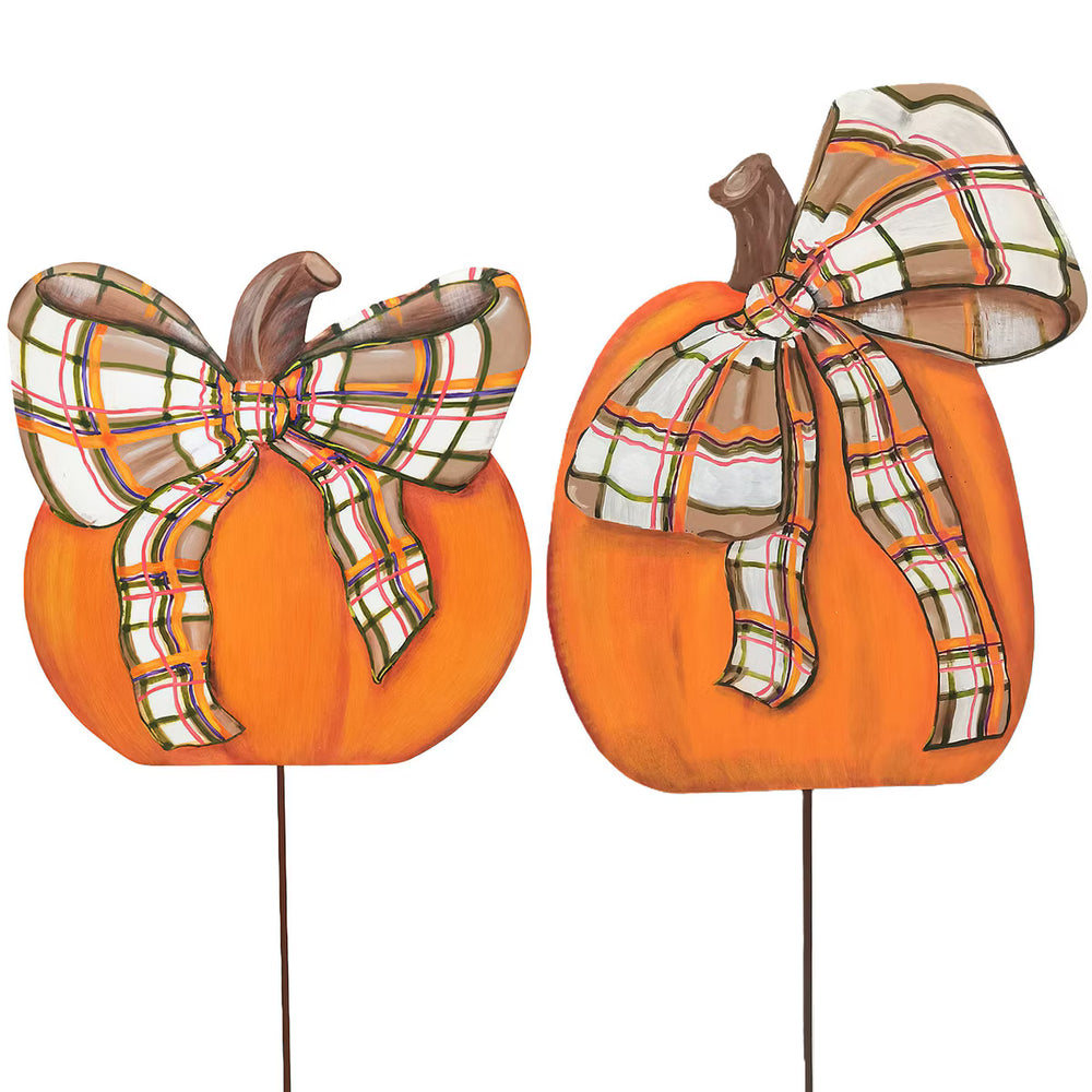 Two orange pumpkin yard signs with brown stems and large plaid bows in beige, white, orange, and green, mounted on thin stakes against a white background.