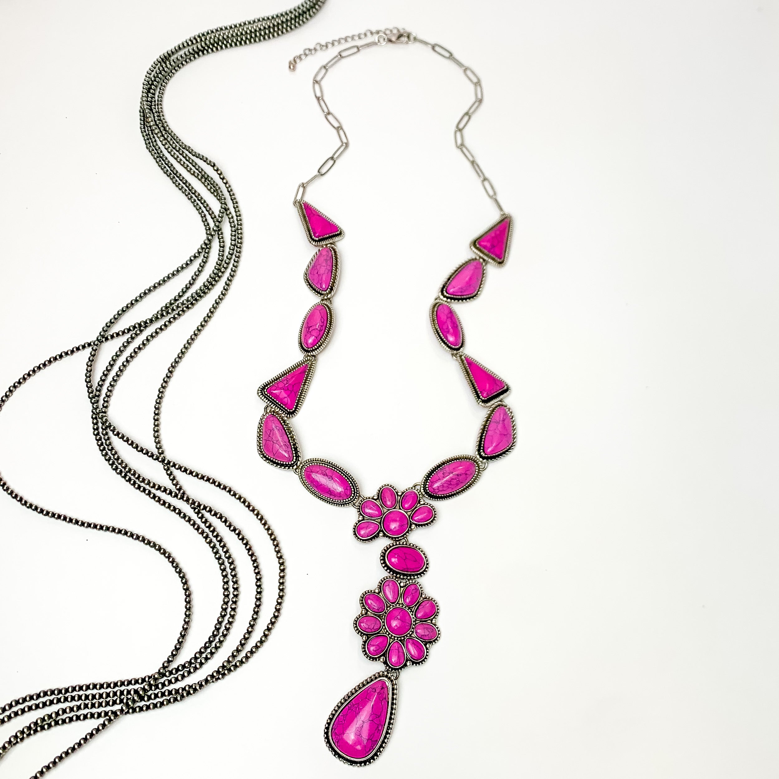 Multi stoned long necklace in pink with a dangling flower cluster. Pictured on a white background with Navajo pearl stands. 