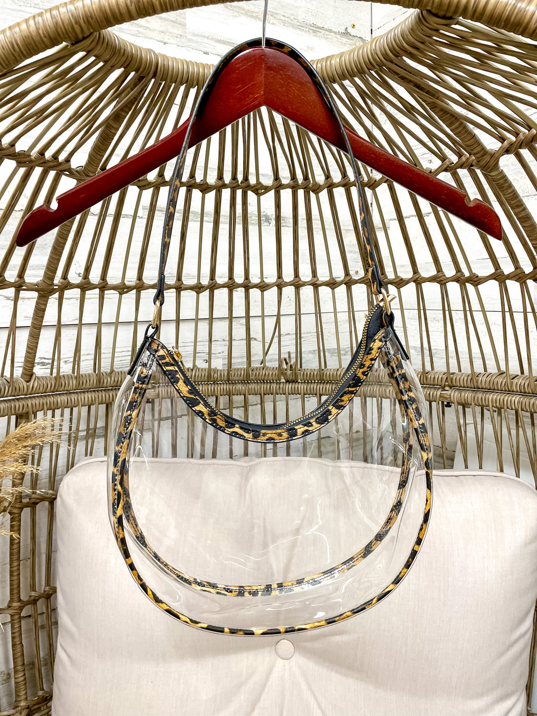 Clear stadium with leopard trim hanging from a wicker chair on a hanger. 