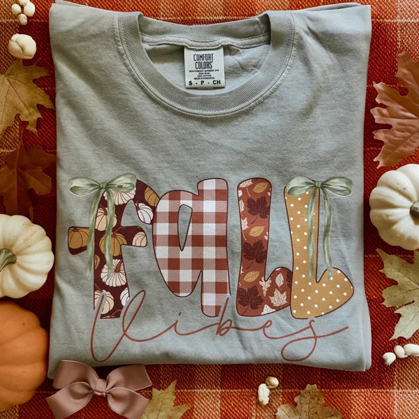 Gray t-shirt with 'Fall Vibes' design on a red checkered tablecloth with pumpkins and leaves.