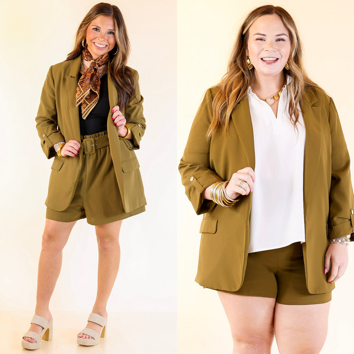 Two women wearing matching green outfits with olive green blazers and shorts on a plain background.